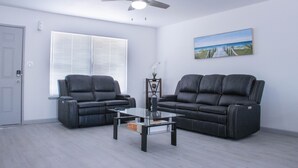 A living room with two black leather sofas, a glass coffee table, a ceiling fan, a window with blinds, and a painting of a beach scene. - Beautiful and cozy house in Las Vegas (Las Vegas)