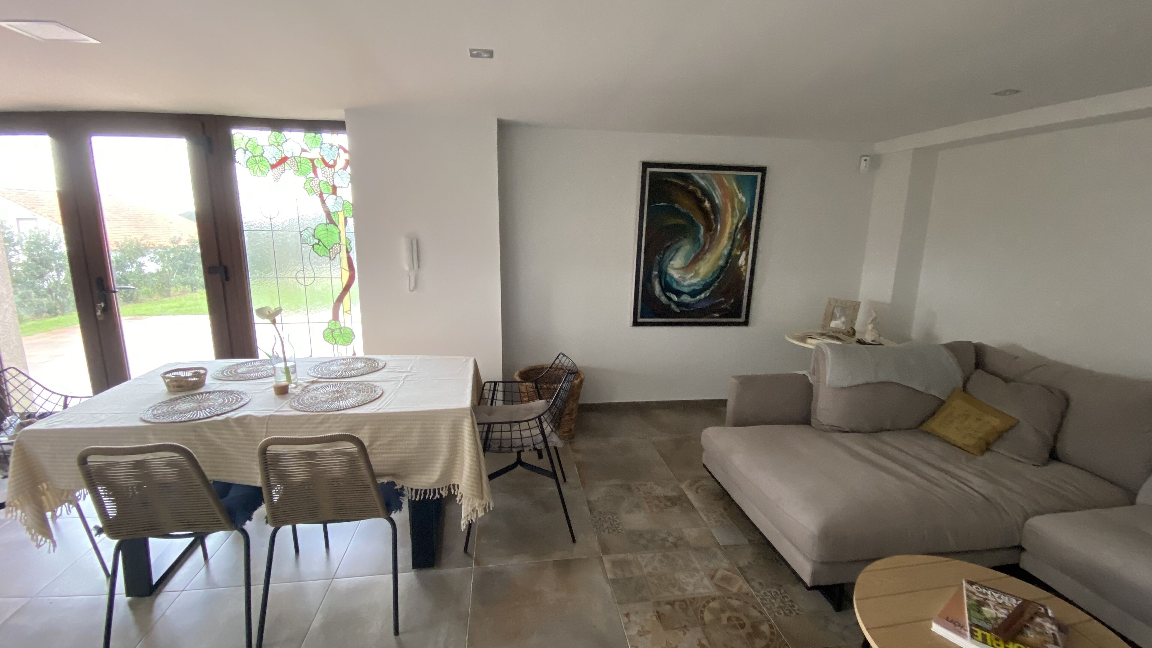Ein Wohnzimmer mit einer Couch, einem Esstisch mit Stühlen und einem großen, abstrakten Gemälde an der Wand.