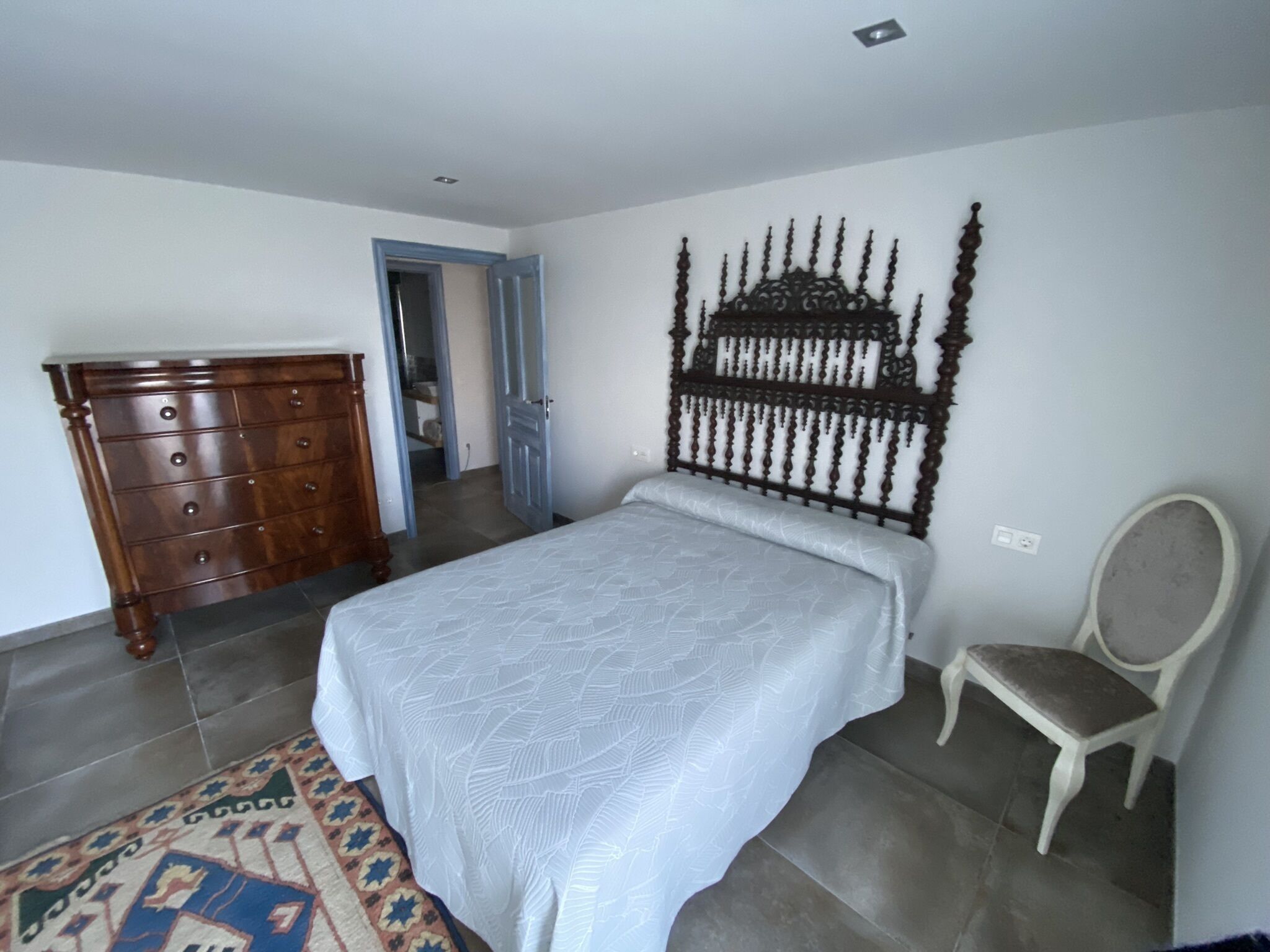 A bedroom with a bed, a wooden dresser, a chair, and a decorative wall headboard.