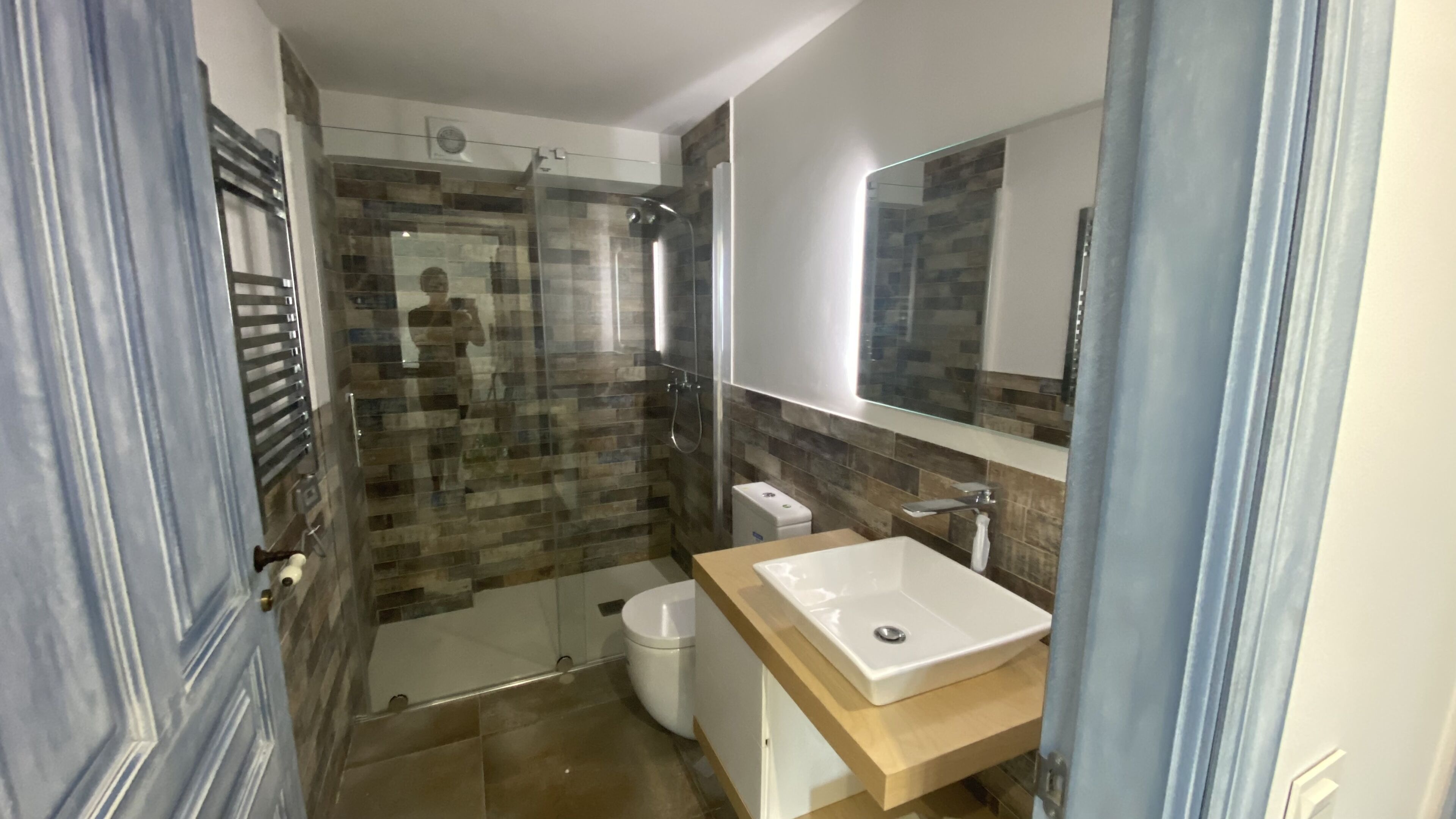 Een moderne badkamer met een glazen douchecabine, een wit toilet en een houten wastafelmeubel met een wastafel.