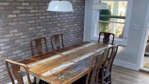 A dining area with a wooden table and chairs, a brick wall, and a window with a view.