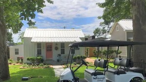 A golf cart parked in front of a house with a white exterior and a red door.