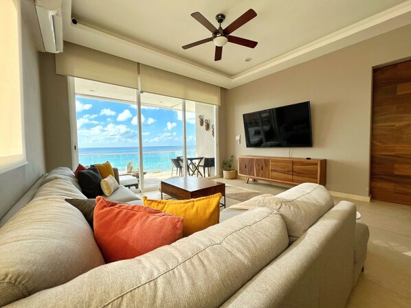 A modern living room with a large sofa, a flat-screen TV, and a ceiling fan.