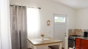 Eine kleine Küche mit Herd, Backofen und einem Fenster mit Blick auf Grünflächen. Ein Tisch mit zwei Stühlen und einer Vase mit Blumen steht darin.