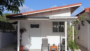 Ein kleines Haus mit weißer Fassade, rotem Dach und einer Tür mit der Aufschrift "A73". Vor der Tür steht ein kleiner Tisch mit Stühlen, und man sieht Blumentöpfe.