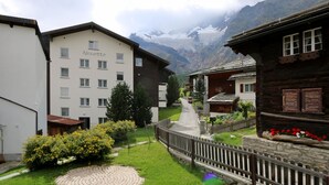 Un hôtel appelé Alouette, avec un chemin de pierre menant à l’entrée, entouré de verdure et avec des montagnes en arrière-plan.