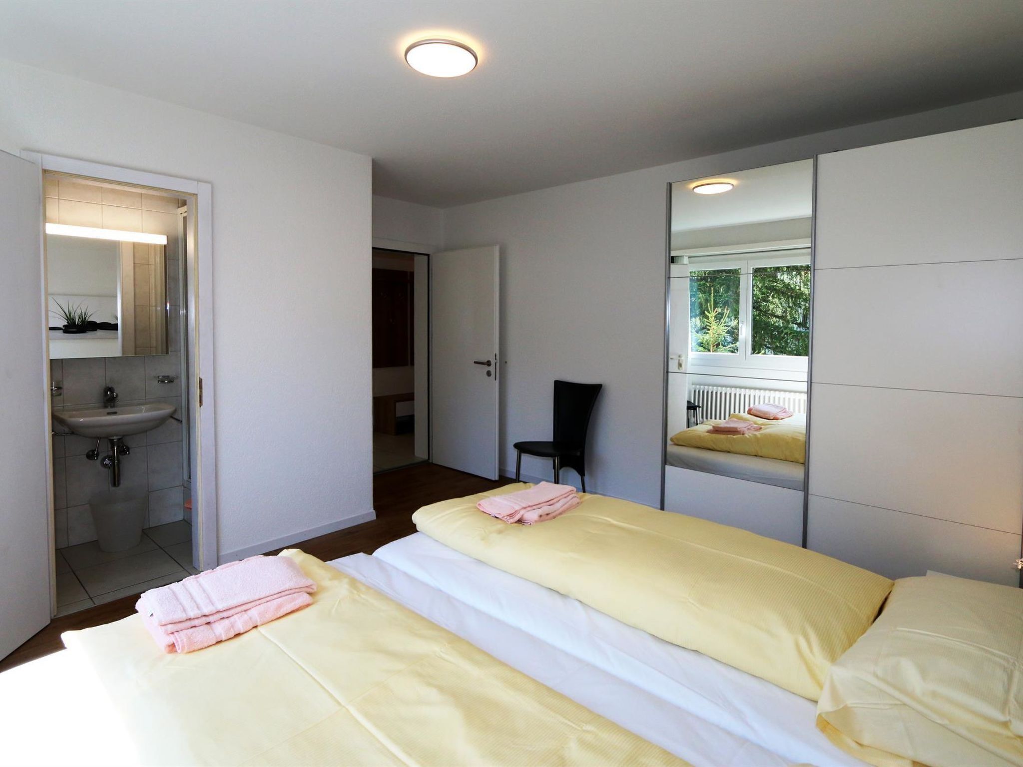 Une chambre avec deux lits, une salle de bain avec un lavabo et un miroir qui reflète la pièce.