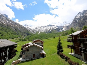 A mountain lodge with a stone exterior, wooden balconies, and a view of snow-capped mountains.