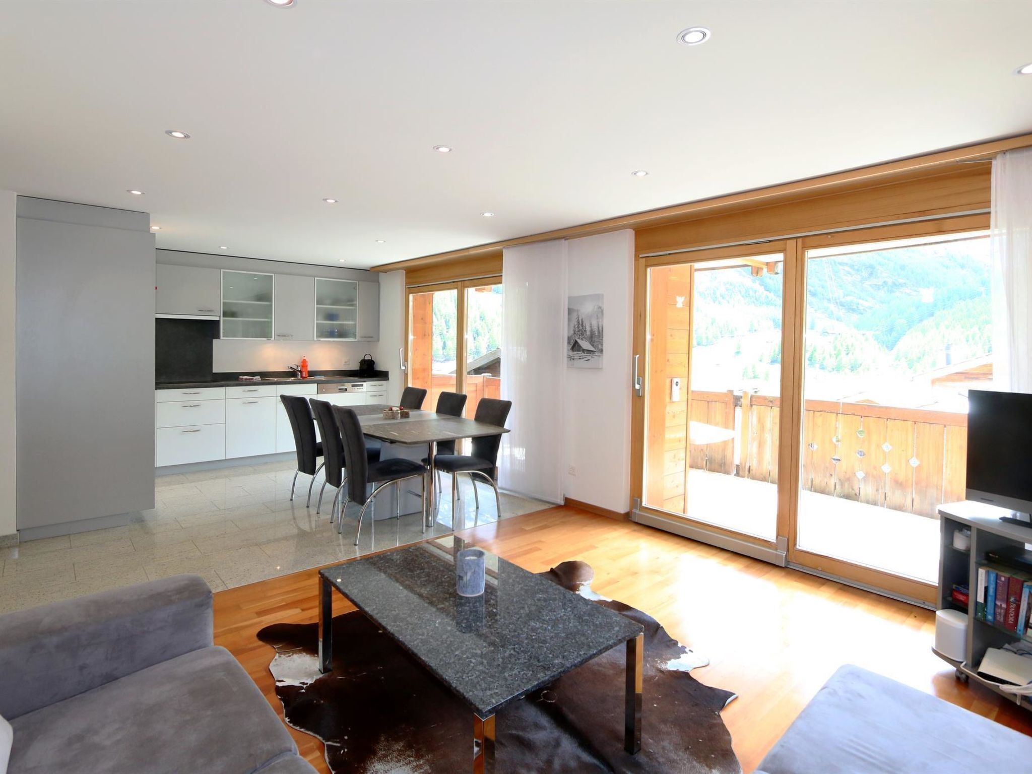 Una sala de estar moderna con comedor, cocina y un amplio ventanal corredera que da a una terraza.