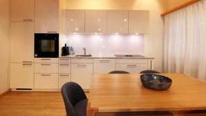 Une cuisine moderne avec des meubles blancs, un four noir et une table à manger en bois sur laquelle est posé un saladier.