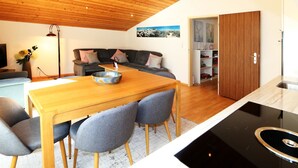 Une cuisine moderne avec un plafond en bois, un coin repas avec une table et des chaises, et un salon avec un canapé et un tableau au mur.