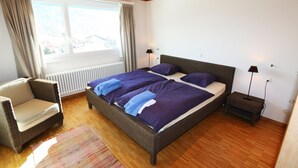 Ein Schlafzimmer mit einem großen Bett, einem Sessel, einem Nachttisch und einem Fenster.