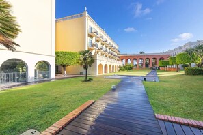 A courtyard with a wooden pathway, palm trees, and a building with arched windows and balconies. - Vilamoura Lake (Quarteira)