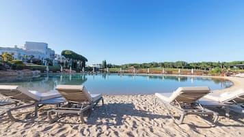 A poolside area with lounge chairs, a sandy beach, and a clear blue sky.