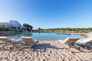A poolside area with lounge chairs, a sandy beach, and a clear blue sky. - Vilamoura Lake (Quarteira)