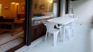 Ein Essbereich mit einem weißen Tisch und Stühlen, einer hölzernen Bank und Blick durch eine Glastür in einen Raum mit Schreibtisch und Stuhl.