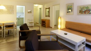 Ein modernes Wohnzimmer mit einer Couch, Sesseln, einem Esstisch und einer Küchenzeile im Hintergrund.