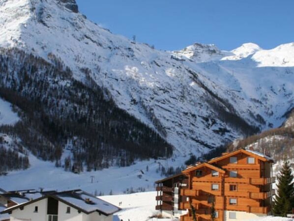 A wooden multi-story building with balconies, surrounded by snow-covered mountains and clear skies. - Apartment Aramis by Interhome (Saas-Fee)