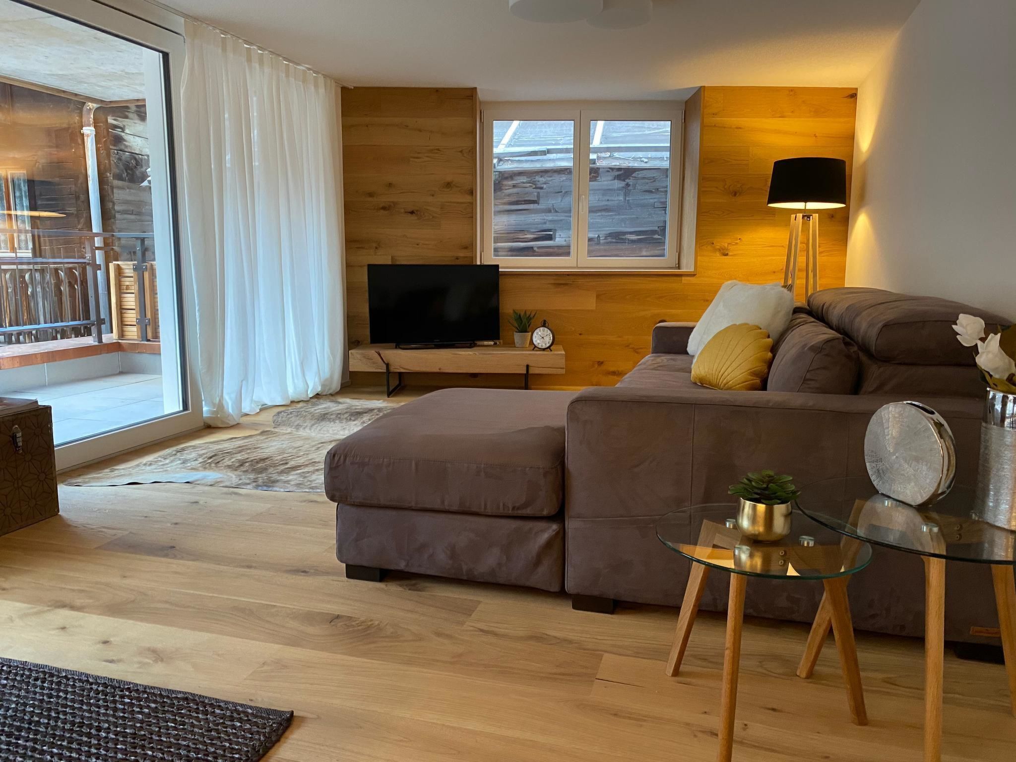 Een moderne woonkamer met een grote hoekbank, een glazen salontafel en een televisie op een houten dressoir.