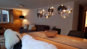 Ett modernt vardagsrum med ett matbord i trä, en svart soffa och en hängande, sfärisk lampa.