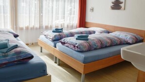 A hotel room with two beds, each with a blue blanket and pillows, a wooden headboard, a white sink, and a window with sheer curtains. - Apartment Heidi by Interhome (Saas-Fee)