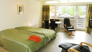 A hotel room with two beds, a dining table with chairs, a TV, and a view of the outside. - Cristal by Interhome (Saas-Fee)