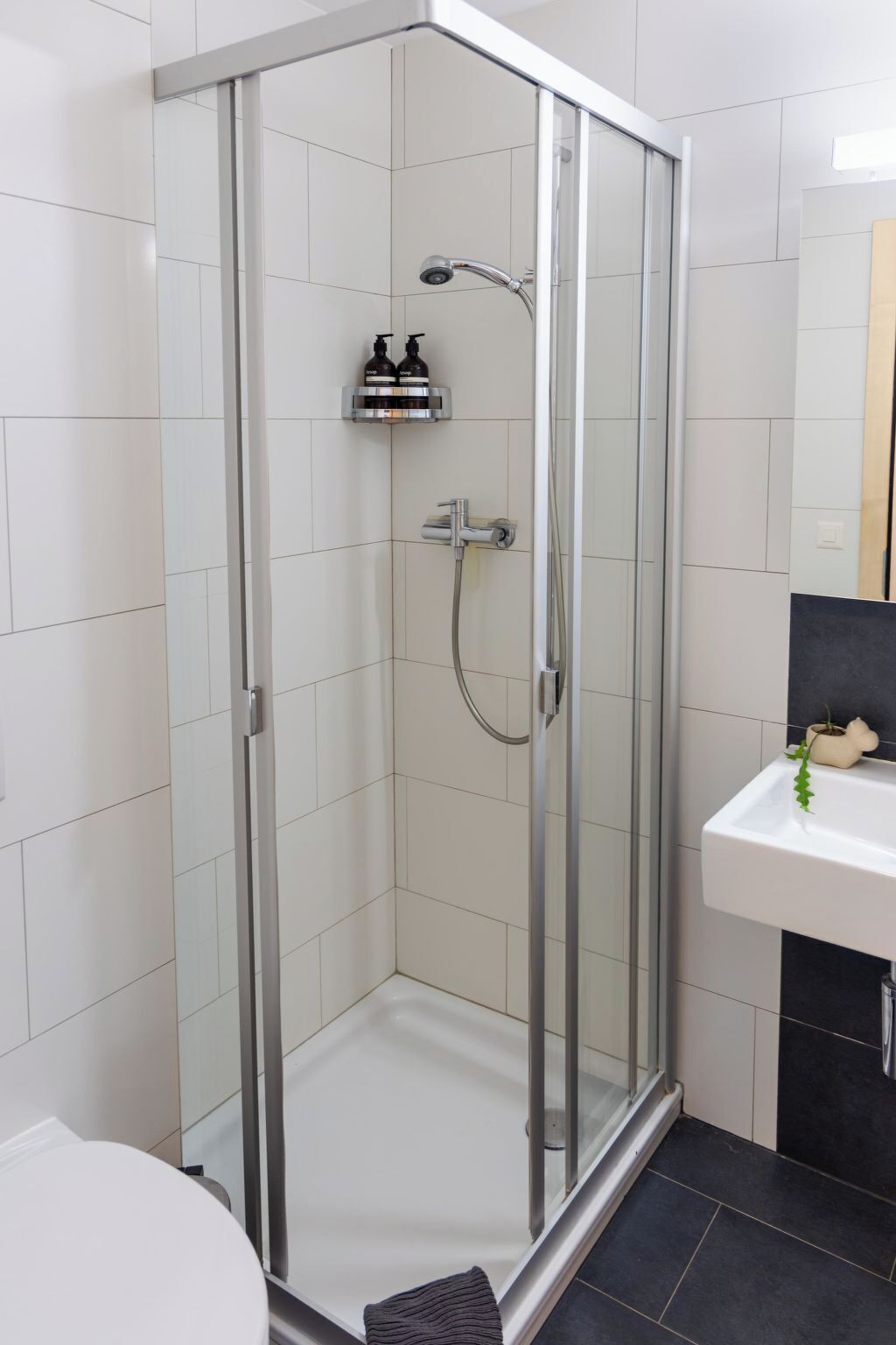 Un box de ducha moderno con puerta de vidrio, un cabezal de ducha manual y un grifo empotrado.
