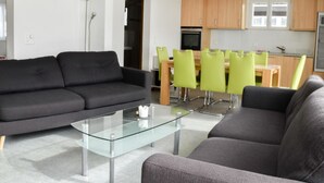 A modern living room with a glass coffee table, two grey sofas, and a dining area with green chairs and wooden tables. - Apartment Heidi by Interhome (Saas-Fee)