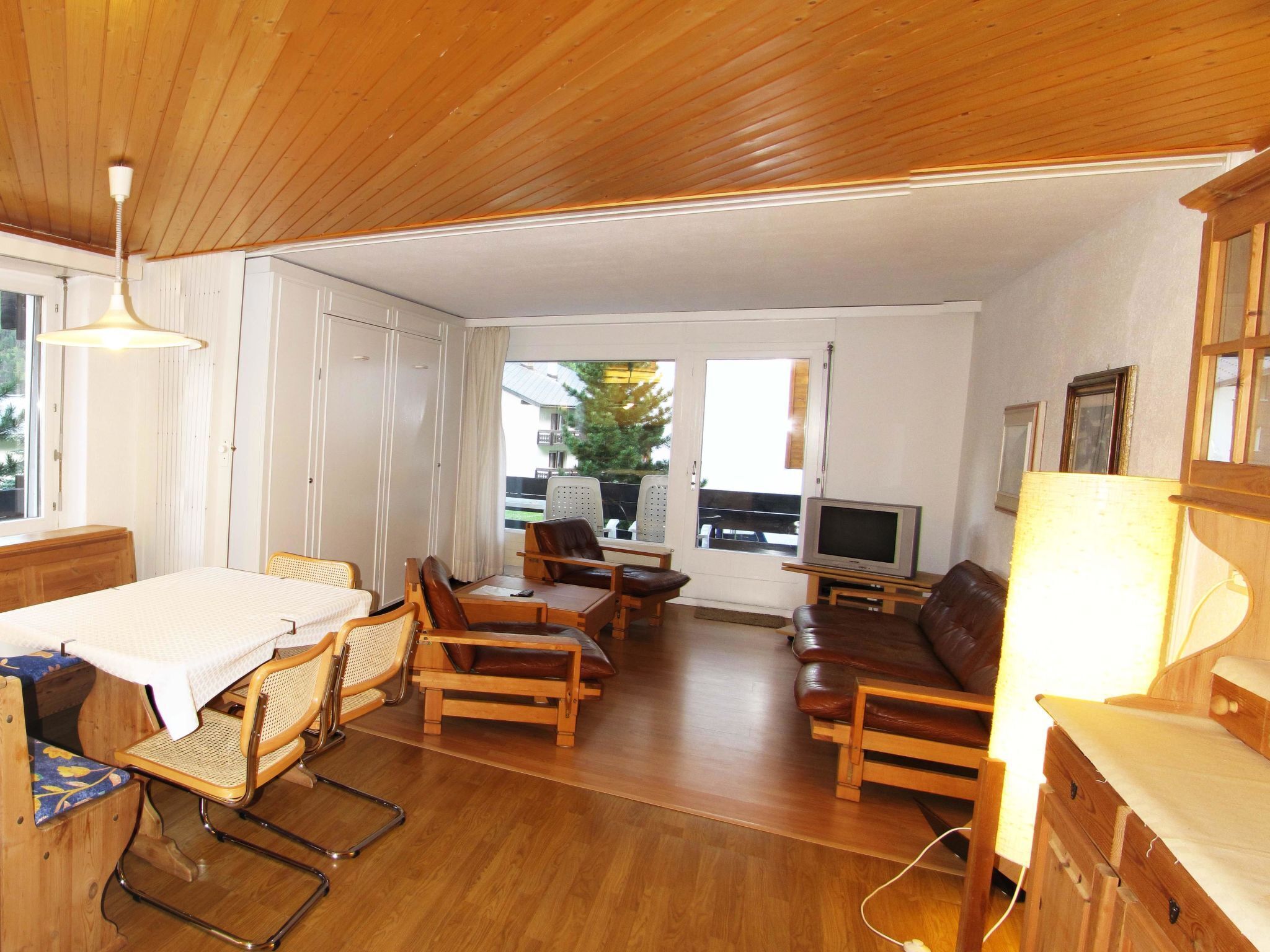 Ett mysigt vardagsrum med trämöbler, en tv och en matplats med bord och stolar.