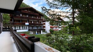 A multi-story building with balconies, surrounded by greenery and mountains in the background.