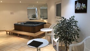 Een moderne badkamer met een bubbelbad, een spiegel, een potplant en een klein tafeltje.