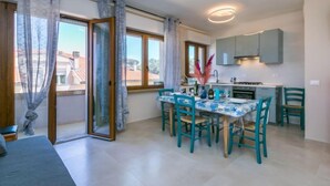 A modern kitchen with a dining table and chairs, large windows with curtains, and a view of the outside. - Marequì by Interhome (San Vincenzo)