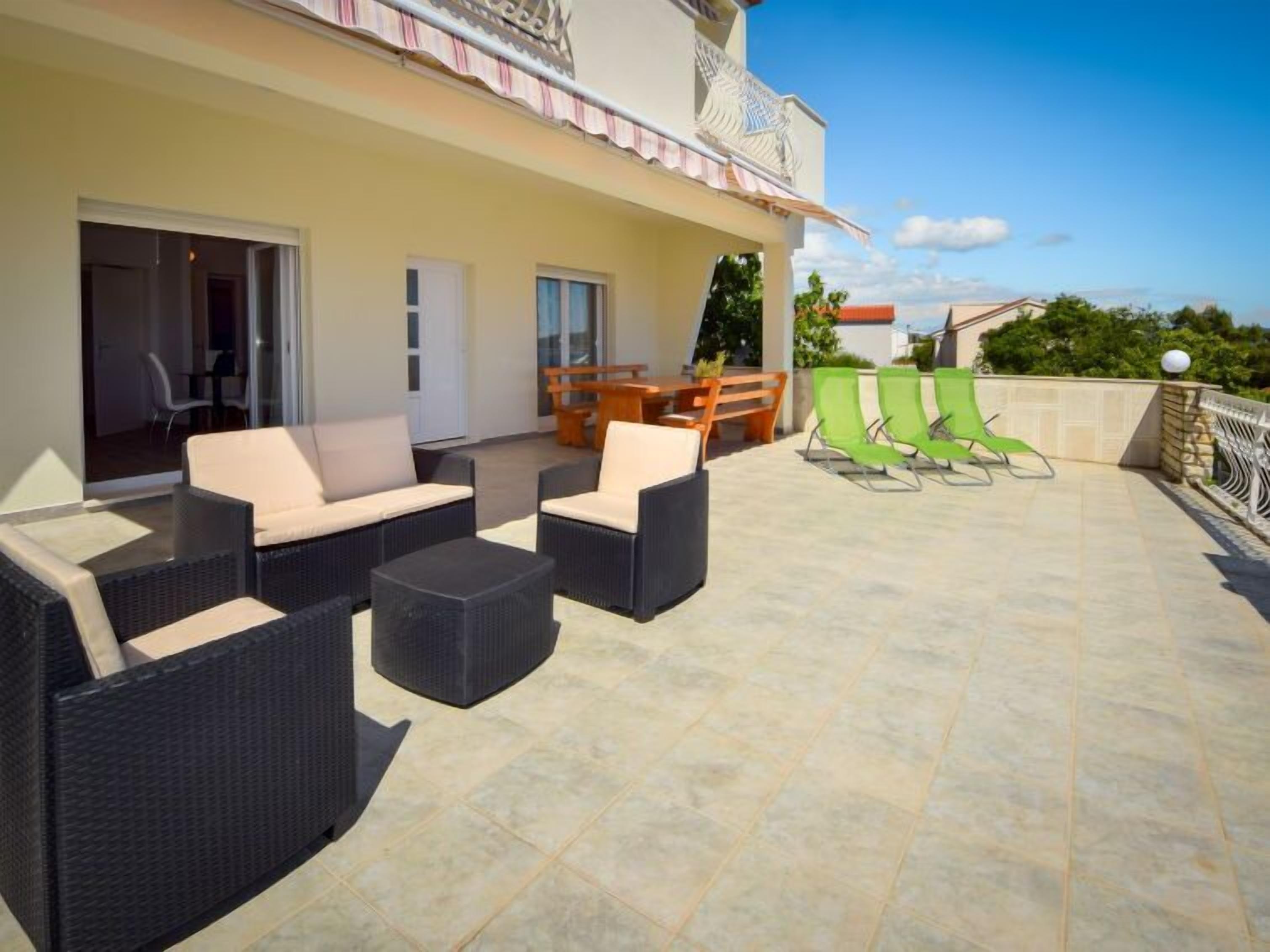 Un espace extérieur aménagé, abrité et doté de mobilier en osier et d’une table, une porte vitrée donnant accès à un espace intérieur, et une vue sur les environs.