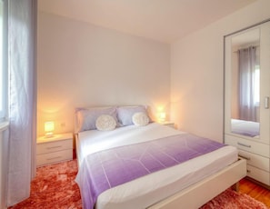 Un dormitorio con cama, mesitas de noche, un espejo y una ventana con cortinas.