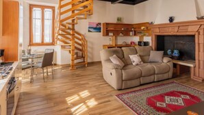 Una sala de estar acogedora con una escalera espiral de madera, un sofá, una chimenea y una zona de cocina con suelo de madera.