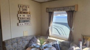 Un rincón acogedor con un área de descanso con cojines, una pequeña mesa redonda preparada para dos personas y una ventana con cortinas.