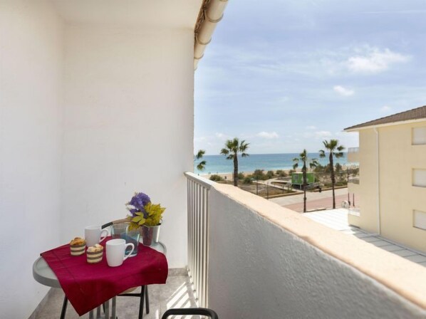 Un balcó amb una taula preparada per a dues persones, un vas amb flors i vista a la platja i l'oceà.