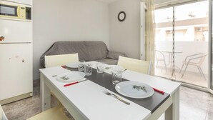 A compact kitchen with a dining table set for two, a refrigerator, and a sofa in the background. - Abanicos by Interhome (Peñiscola)