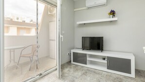 A modern living room with a sliding glass door leading to a balcony, a flat-screen TV on a white console, and a wall-mounted air conditioner. - Abanicos by Interhome (Peñiscola)