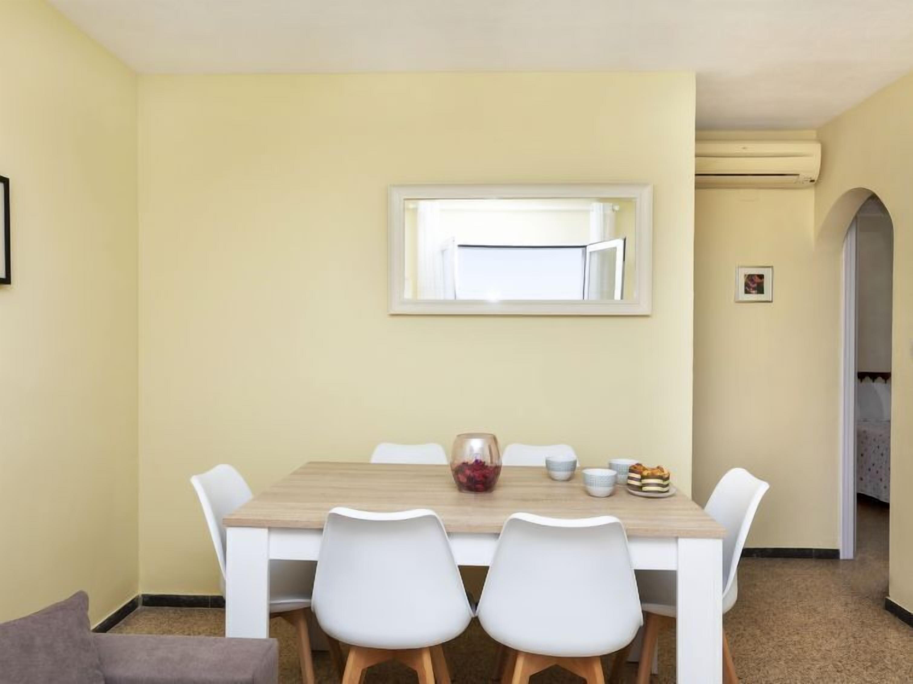 Un comedor con una mesa de madera, sillas blancas y un florero con flores.