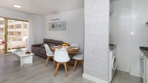 A modern apartment with a dining area, a sofa, a washing machine, and a view of the outside balcony. - Peñismar I by Interhome (Peñiscola)