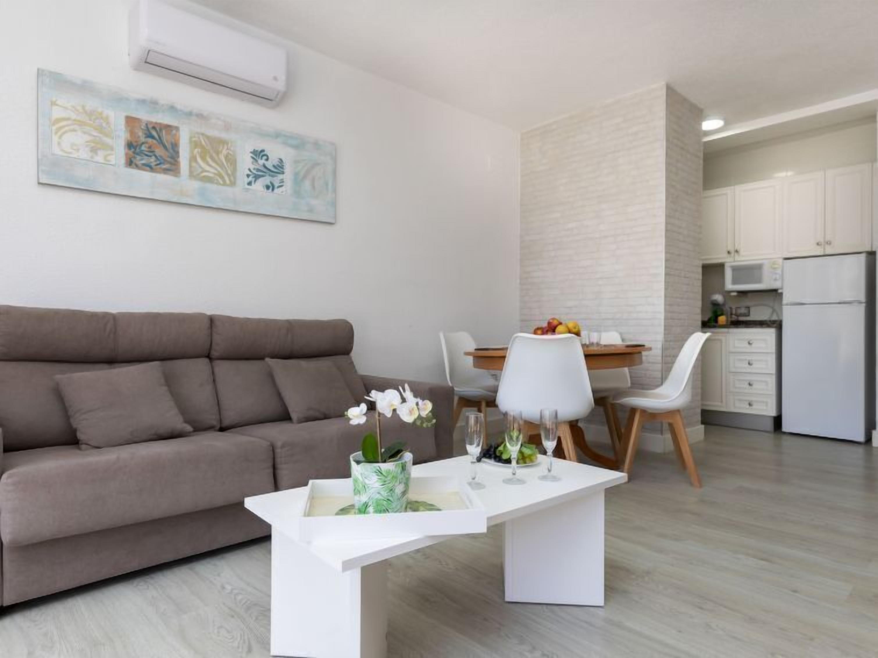 A modern living room with a sofa, a dining table with chairs, and a kitchen area with cabinets and appliances.
