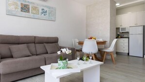 A modern living room with a sofa, a dining table with chairs, and a kitchen area with cabinets and appliances. - Peñismar I by Interhome (Peñiscola)