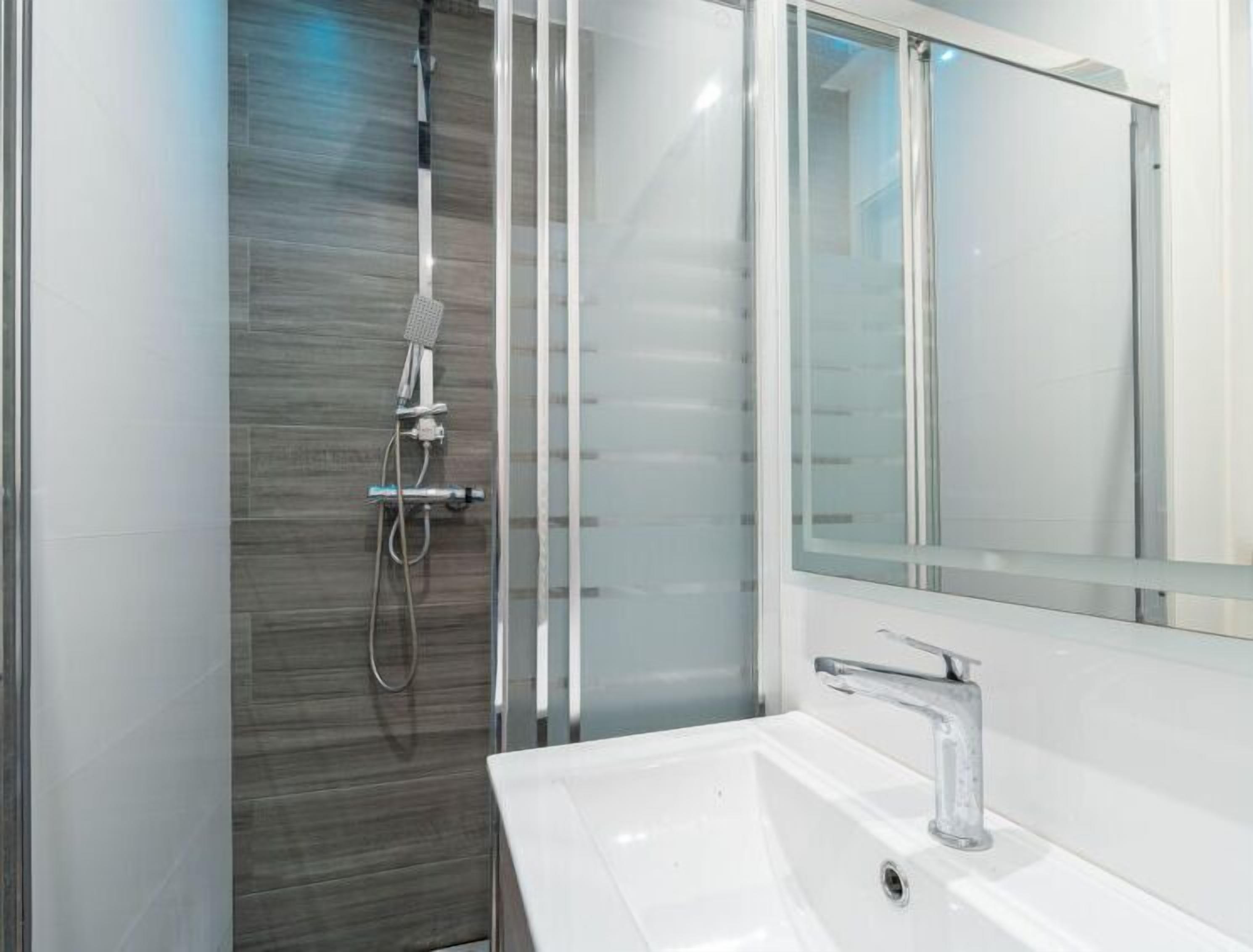 A modern bathroom with a glass shower enclosure, a white sink, and a large mirror.