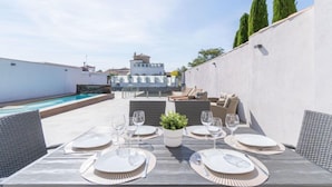 Un espace extérieur aménagé pour les repas, avec une piscine, des murs blancs et une vue sur un bâtiment en arrière-plan.