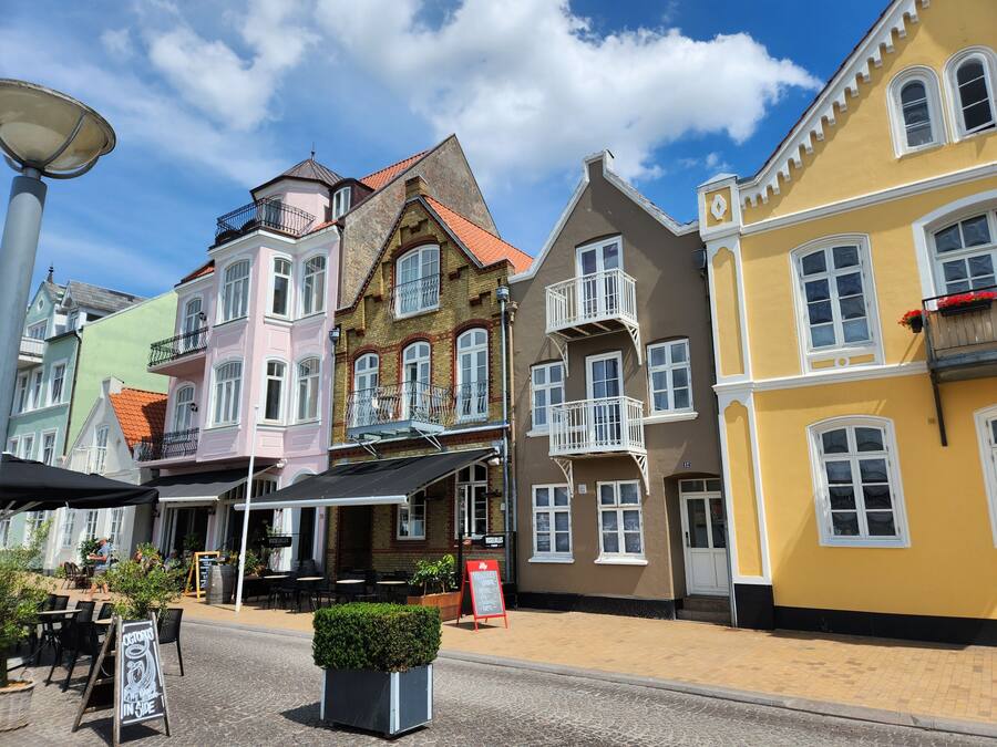 Une rue bordée de bâtiments aux couleurs vives, avec des terrasses et une enseigne.
