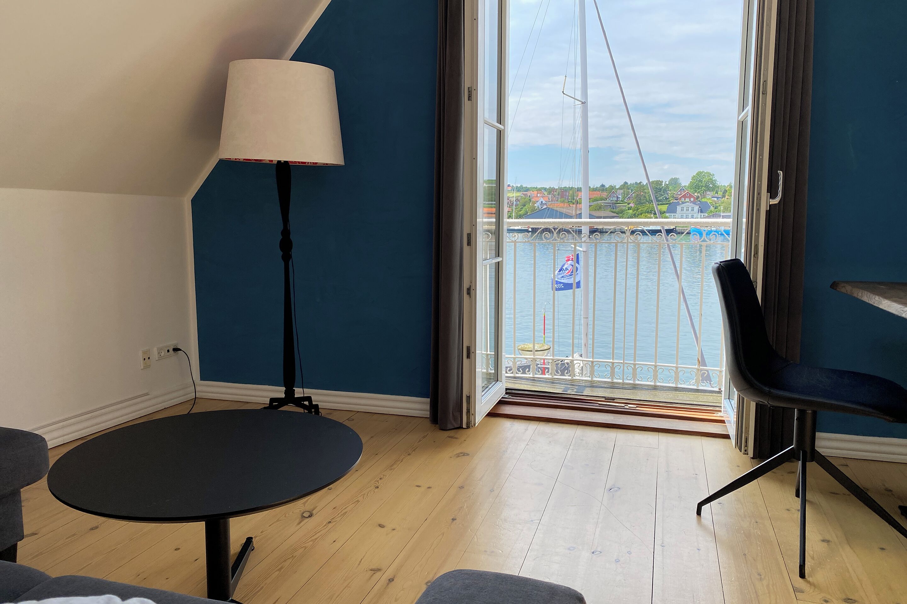 A room with a large window, a round table, a chair, and a lamp.