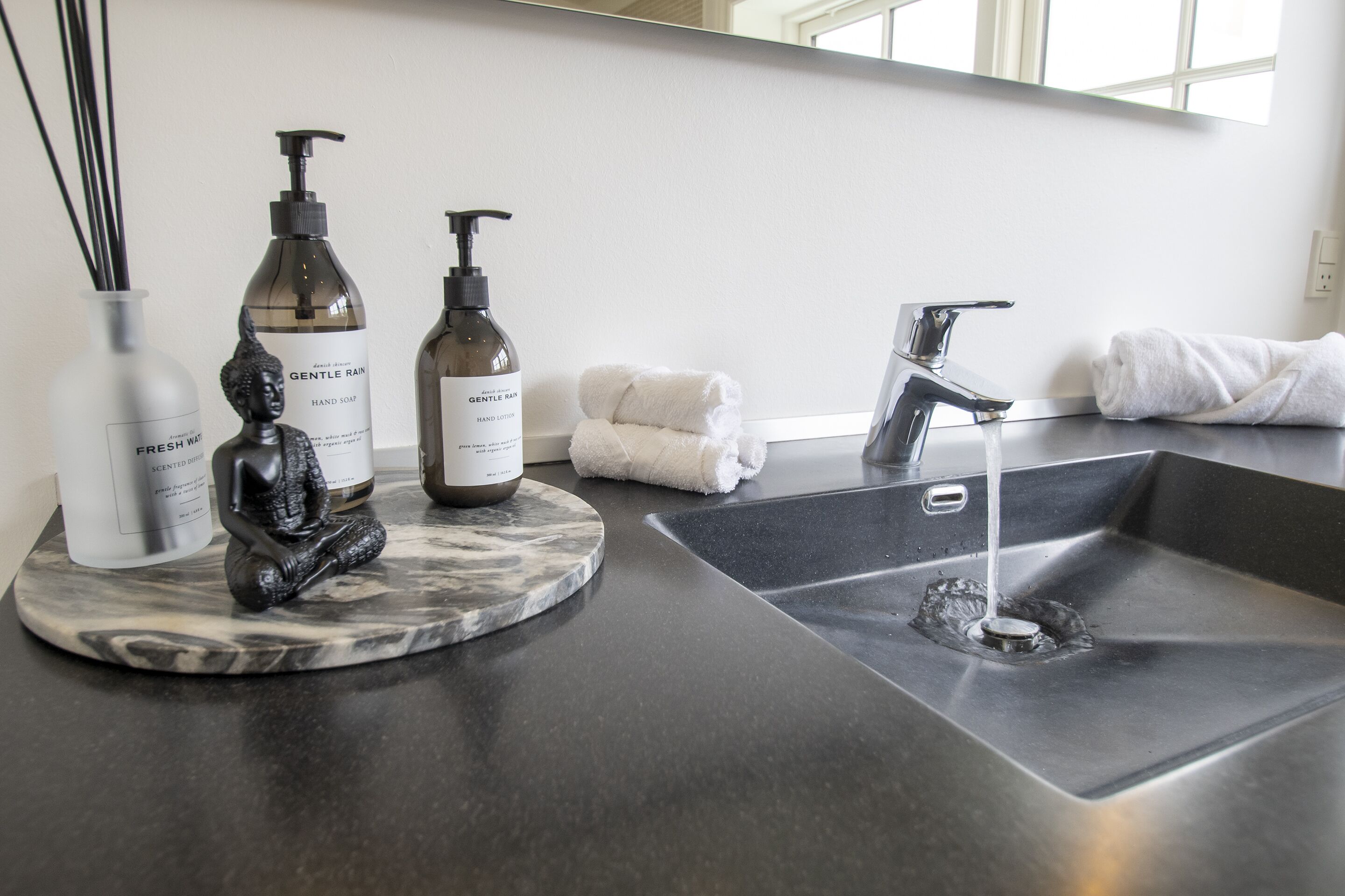 A bathroom counter with hand soap, a hand lotion dispenser, a towel, and a marble tray.