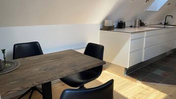 Una cocina moderna con tragaluz, un comedor con mesa de madera y sillas negras, y una pequeña isla con un hervidor.