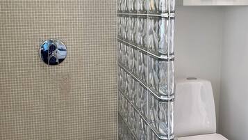 A bathroom with a tiled shower wall, a toilet, and a white cabinet.